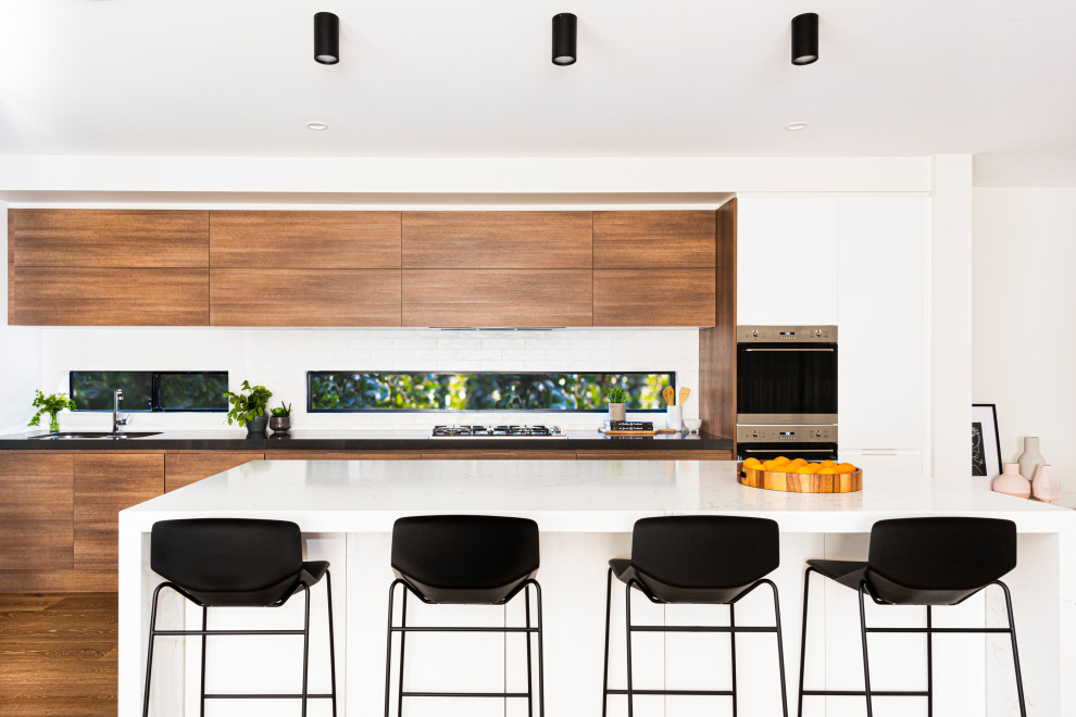 Idée de décoration pour une cuisine parallèle design en bois brun avec un évier encastré, un placard à porte plane, fenêtre, un électroménager en acier inoxydable, un sol en bois brun, îlot, un sol marron et un plan de travail blanc.