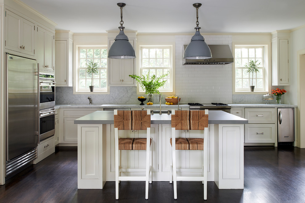Kitchen - transitional l-shaped dark wood floor and brown floor kitchen idea in Philadelphia with shaker cabinets, white cabinets, white backsplash, subway tile backsplash, stainless steel appliances, an island and gray countertops