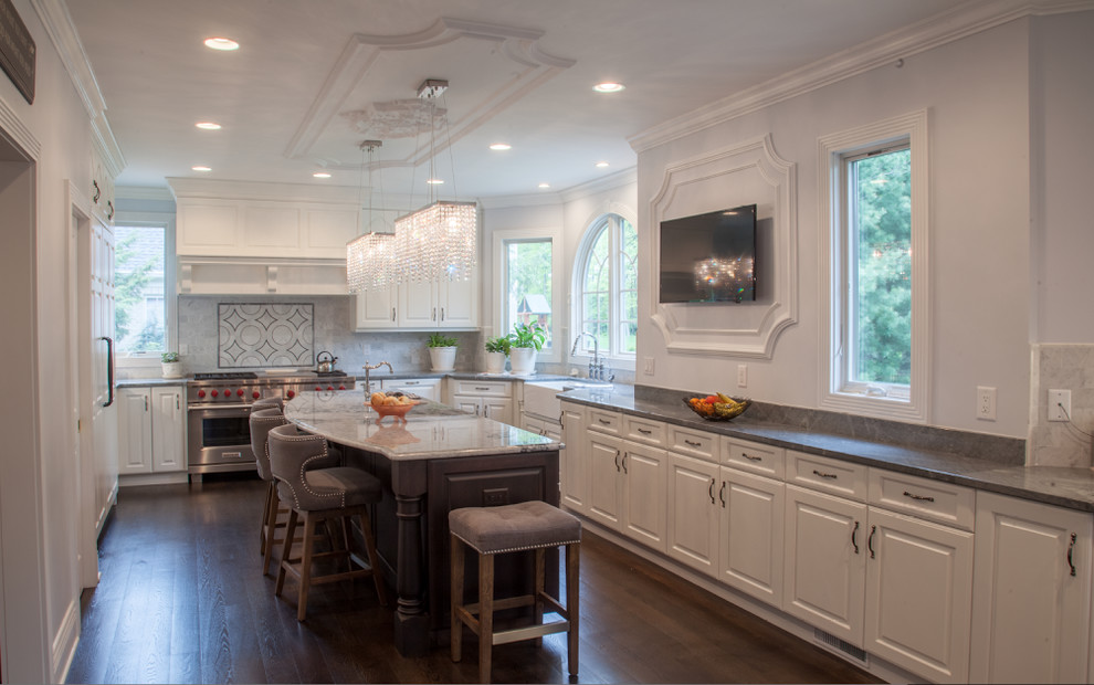 Example of a large transitional u-shaped dark wood floor and brown floor enclosed kitchen design in Cleveland with a farmhouse sink, raised-panel cabinets, white cabinets, marble countertops, gray backsplash, marble backsplash, paneled appliances and an island