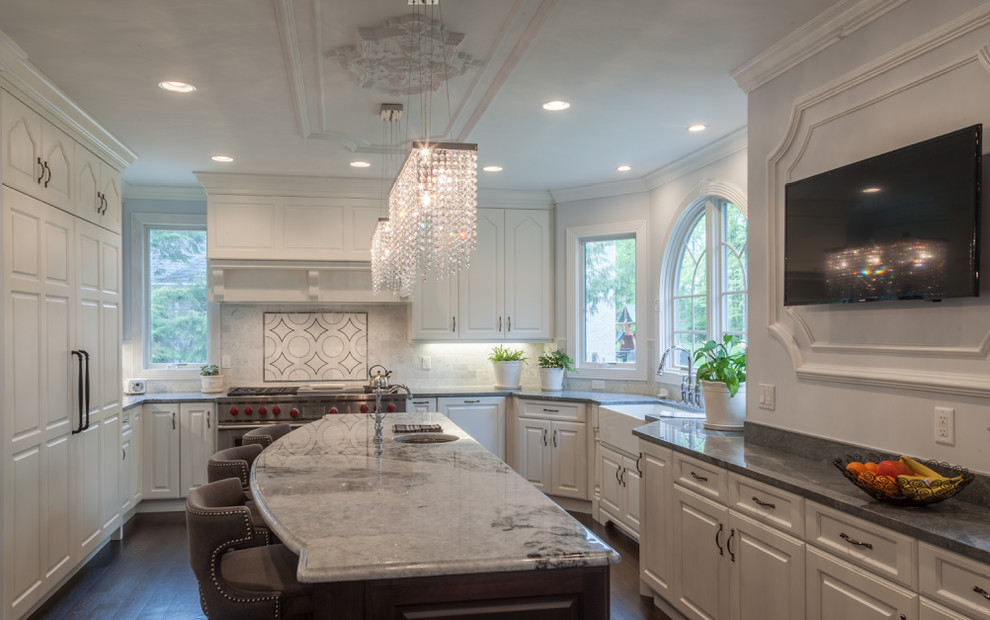 Example of a large transitional u-shaped dark wood floor and brown floor enclosed kitchen design in Cleveland with a farmhouse sink, raised-panel cabinets, white cabinets, marble countertops, gray backsplash, marble backsplash, paneled appliances and an island