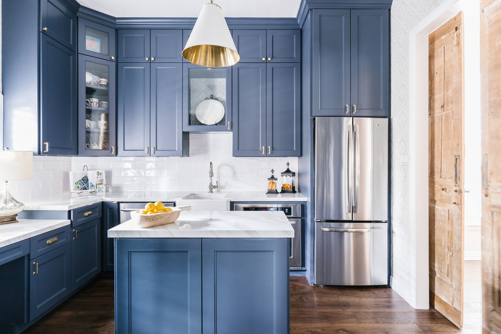 Klassische Küche in L-Form mit Landhausspüle, Schrankfronten im Shaker-Stil, blauen Schränken, Küchenrückwand in Weiß, Küchengeräten aus Edelstahl, braunem Holzboden, Kücheninsel, braunem Boden und weißer Arbeitsplatte in Houston
