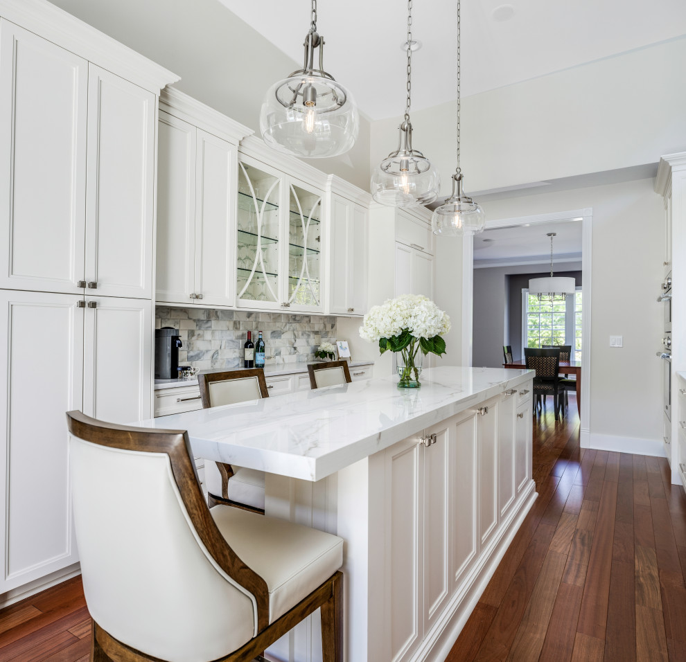 This is an example of a large classic galley enclosed kitchen in Detroit with a submerged sink, raised-panel cabinets, white cabinets, engineered stone countertops, white splashback, marble splashback, integrated appliances, medium hardwood flooring, an island, red floors and white worktops.