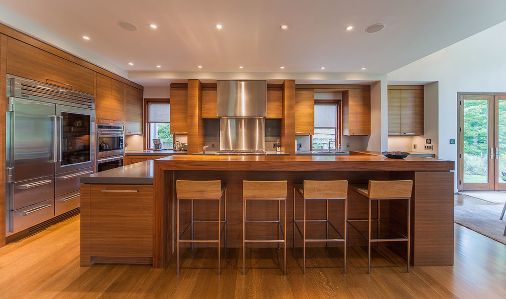 Moderne Wohnküche in U-Form mit flächenbündigen Schrankfronten, hellbraunen Holzschränken, Küchengeräten aus Edelstahl, braunem Holzboden und Kücheninsel in Toronto