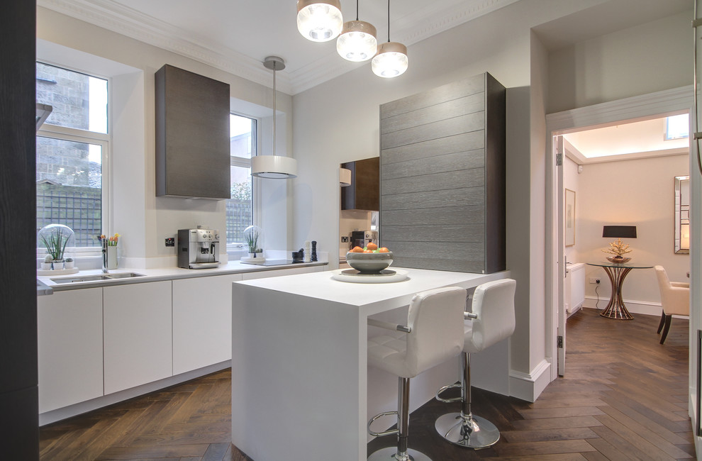 Small contemporary galley kitchen in Glasgow with a double-bowl sink, flat-panel cabinets, white cabinets, medium hardwood flooring, a breakfast bar, brown floors, white worktops and integrated appliances.
