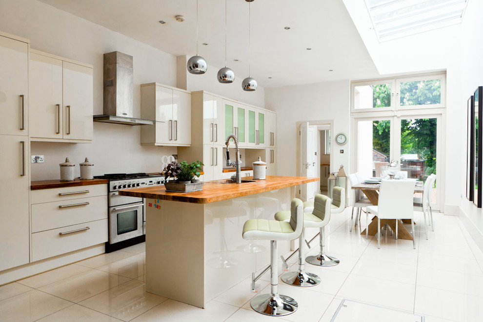 This is an example of a medium sized contemporary single-wall kitchen/diner in Dublin with a submerged sink, flat-panel cabinets, white cabinets, wood worktops, white splashback, stainless steel appliances, ceramic flooring and an island.