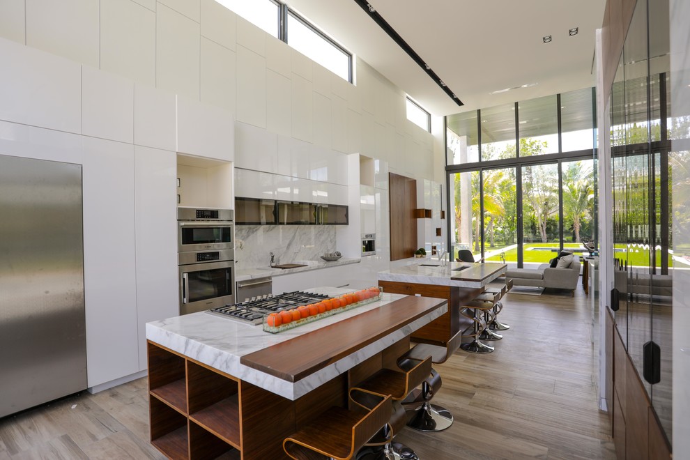 Offene, Zweizeilige Moderne Küche mit flächenbündigen Schrankfronten, weißen Schränken, Küchenrückwand in Grau, Küchengeräten aus Edelstahl, hellem Holzboden, zwei Kücheninseln, beigem Boden und grauer Arbeitsplatte in Miami