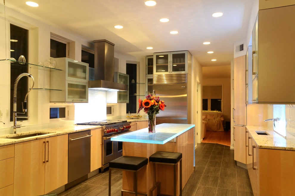Example of a trendy l-shaped eat-in kitchen design in New York with an undermount sink, flat-panel cabinets, light wood cabinets, glass countertops, white backsplash, glass tile backsplash and stainless steel appliances