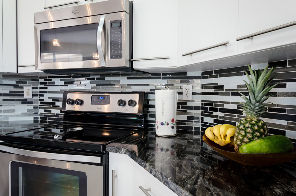 Foto på ett funkis kök, med släta luckor, vita skåp, granitbänkskiva, grått stänkskydd, stänkskydd i glaskakel och rostfria vitvaror