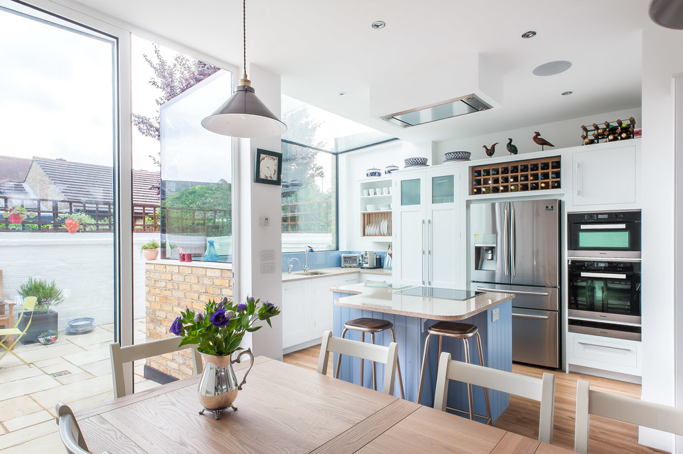Landhaus Wohnküche mit Schrankfronten im Shaker-Stil, weißen Schränken, Küchenrückwand in Blau, braunem Holzboden, Kücheninsel und Küchengeräten aus Edelstahl in London