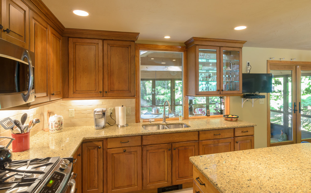 Eat-in kitchen - traditional l-shaped eat-in kitchen idea in Boston with a double-bowl sink, raised-panel cabinets, medium tone wood cabinets, granite countertops, beige backsplash, ceramic backsplash, stainless steel appliances and an island