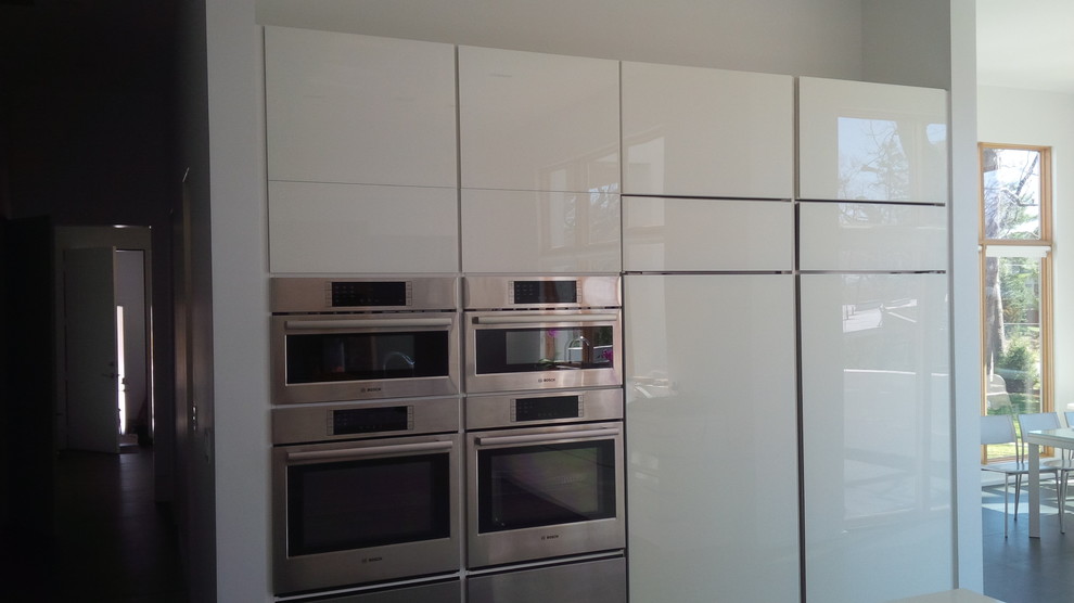 Inspiration for a modern kitchen/diner in New York with a submerged sink, flat-panel cabinets, white cabinets, white splashback, an island and stainless steel appliances.