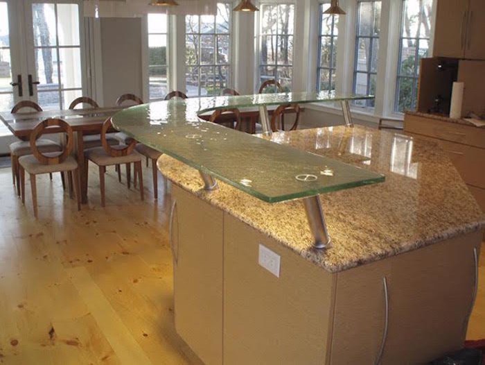 Bild på ett mellanstort funkis kök, med släta luckor, skåp i ljust trä, bänkskiva i glas, ljust trägolv, en köksö och rostfria vitvaror