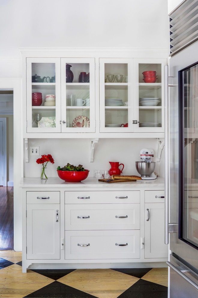 Klassisk inredning av ett mellanstort l-kök, med en integrerad diskho, släta luckor, vita skåp, bänkskiva i rostfritt stål, vitt stänkskydd, stänkskydd i keramik, rostfria vitvaror och målat trägolv