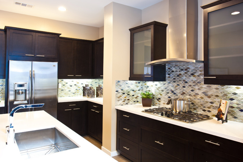 This is an example of a medium sized contemporary l-shaped enclosed kitchen in Orange County with a submerged sink, flat-panel cabinets, dark wood cabinets, engineered stone countertops, multi-coloured splashback, mosaic tiled splashback, stainless steel appliances, light hardwood flooring and an island.