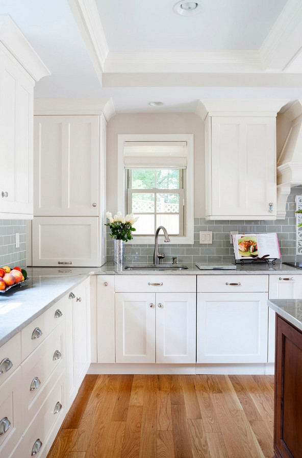 Klassisk inredning av ett kök, med luckor med upphöjd panel, vita skåp, bänkskiva i koppar, grönt stänkskydd, stänkskydd i glaskakel, rostfria vitvaror och mellanmörkt trägolv