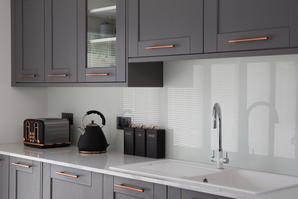 Design ideas for a medium sized modern single-wall kitchen/diner in Other with an integrated sink, shaker cabinets, grey cabinets, marble worktops, white splashback, glass sheet splashback, black appliances and white worktops.