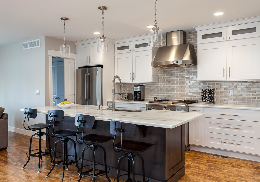 Example of a trendy medium tone wood floor kitchen design in Denver with an undermount sink, shaker cabinets, white cabinets, granite countertops, beige backsplash, subway tile backsplash, stainless steel appliances and an island