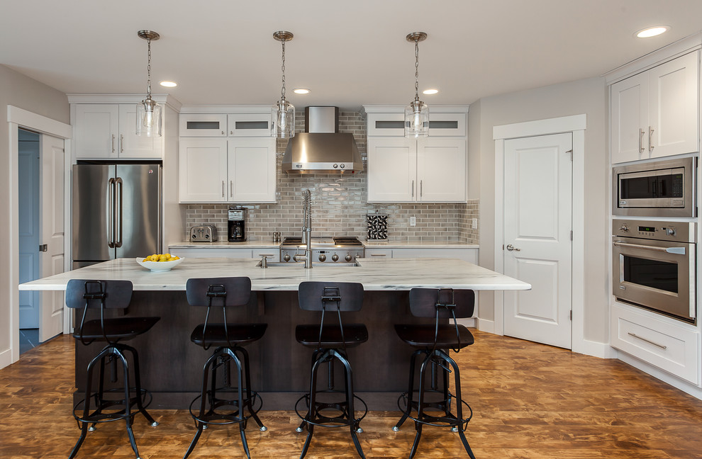 Inspiration for a transitional medium tone wood floor kitchen remodel in Denver with an undermount sink, shaker cabinets, white cabinets, granite countertops, beige backsplash, subway tile backsplash, stainless steel appliances and an island