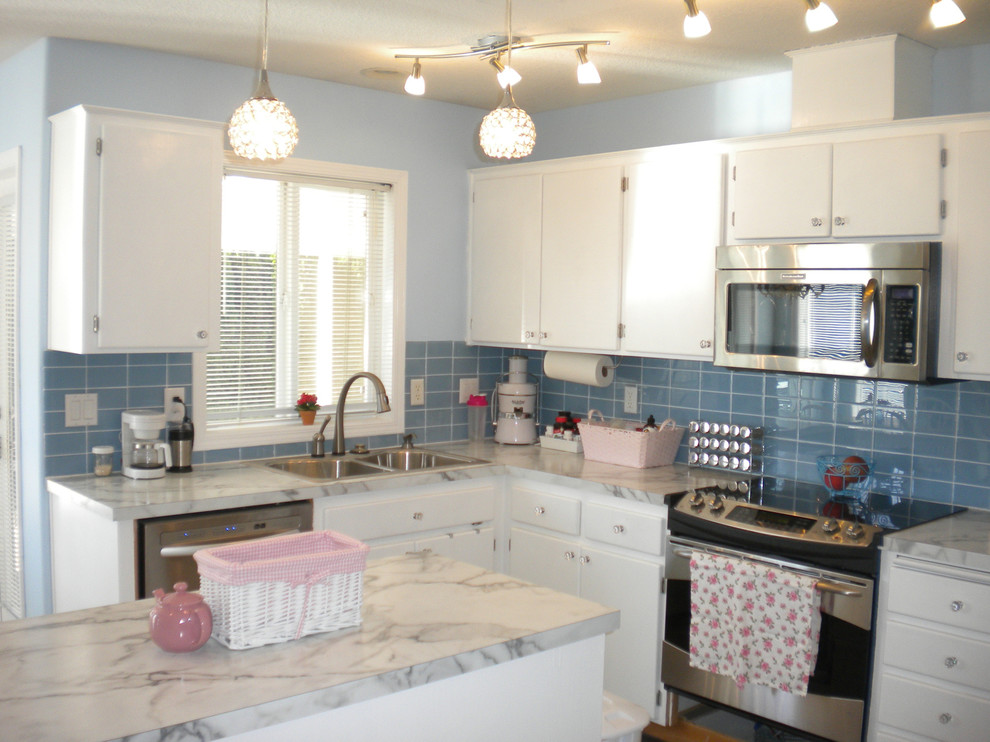 На фото: угловая кухня в стиле неоклассика (современная классика) с обеденным столом, двойной мойкой, белыми фасадами, синим фартуком, фартуком из стеклянной плитки и техникой из нержавеющей стали