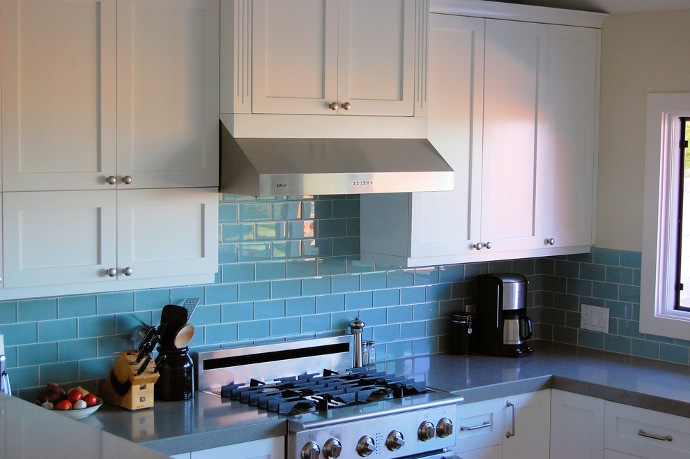 Bild på ett funkis kök, med vita skåp, blått stänkskydd, stänkskydd i glaskakel och rostfria vitvaror