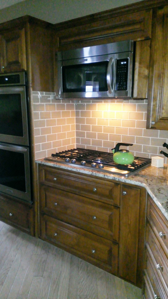 Cette image montre une cuisine américaine traditionnelle avec des portes de placard marrons, une crédence marron, une crédence en carreau de verre et un électroménager en acier inoxydable.
