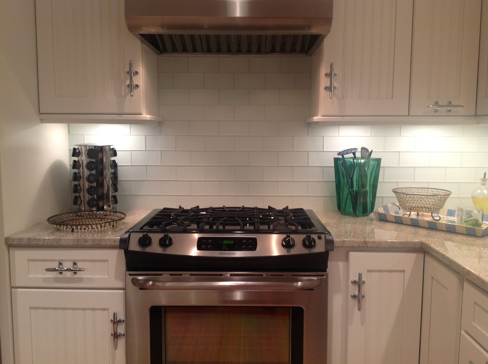 Exemple d'une cuisine américaine chic avec des portes de placard blanches, une crédence blanche, une crédence en carreau de verre et un électroménager en acier inoxydable.