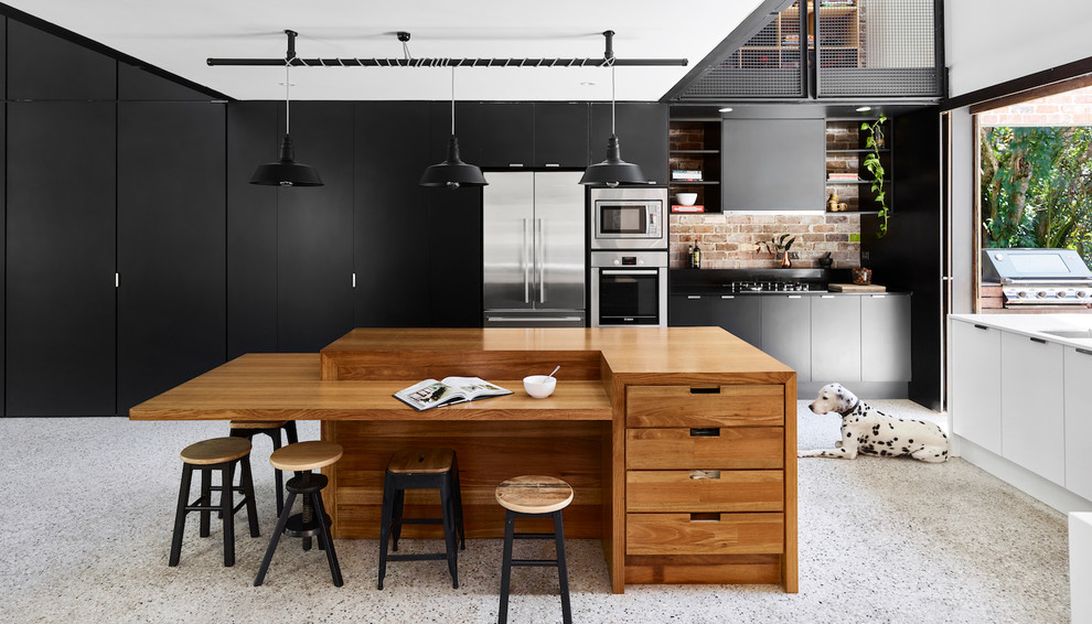 Inspiration for a large industrial l-shaped concrete floor kitchen pantry remodel in Sunshine Coast with an undermount sink, black cabinets, wood countertops, brick backsplash, stainless steel appliances and an island