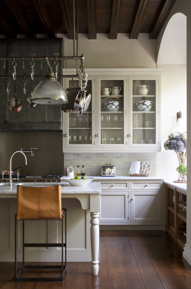 Foto på ett stort vintage kök, med en enkel diskho, luckor med infälld panel, vita skåp, marmorbänkskiva, stänkskydd med metallisk yta, mörkt trägolv och en köksö