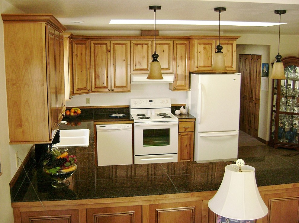 Cette image montre une cuisine américaine traditionnelle en U et bois clair avec un placard avec porte à panneau surélevé, un plan de travail en granite et un électroménager blanc.