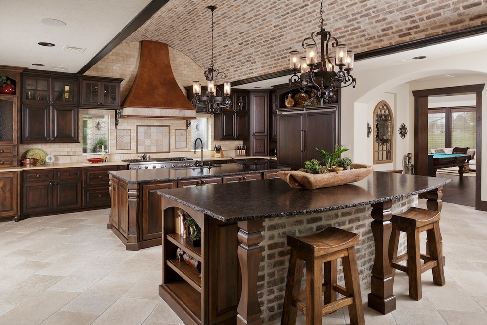 Example of a large tuscan u-shaped porcelain tile kitchen design in Houston with raised-panel cabinets, dark wood cabinets, granite countertops, beige backsplash, porcelain backsplash, paneled appliances and two islands