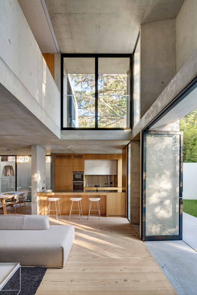 Идея дизайна: параллельная кухня-гостиная в стиле модернизм с плоскими фасадами, фасадами цвета дерева среднего тона, полуостровом и светлым паркетным полом