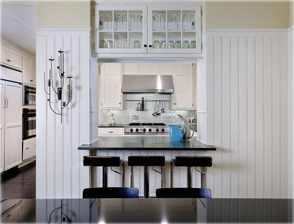 Cette photo montre une petite cuisine chic en U avec un placard à porte plane, des portes de placard blanches, une crédence blanche, un électroménager en acier inoxydable et parquet foncé.