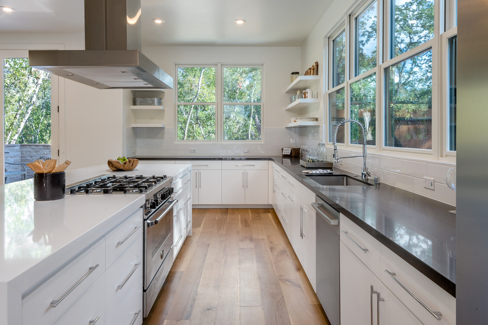 Inspiration for an expansive country kitchen/diner in San Francisco with a single-bowl sink, flat-panel cabinets, white cabinets, engineered stone countertops, white splashback, metro tiled splashback, stainless steel appliances, light hardwood flooring and an island.