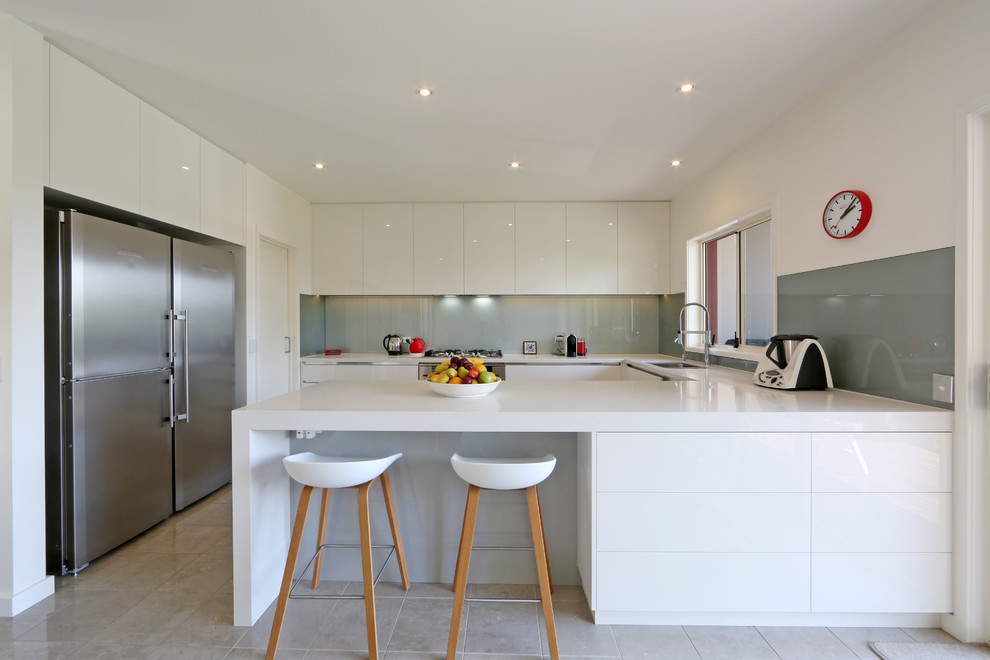 Moderne Küche in U-Form mit flächenbündigen Schrankfronten, weißen Schränken, Küchenrückwand in Grau, Glasrückwand und Küchengeräten aus Edelstahl in Melbourne