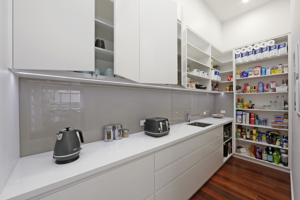 Cette image montre une arrière-cuisine linéaire design avec un évier encastré, un placard à porte plane, des portes de placard blanches et une crédence grise.