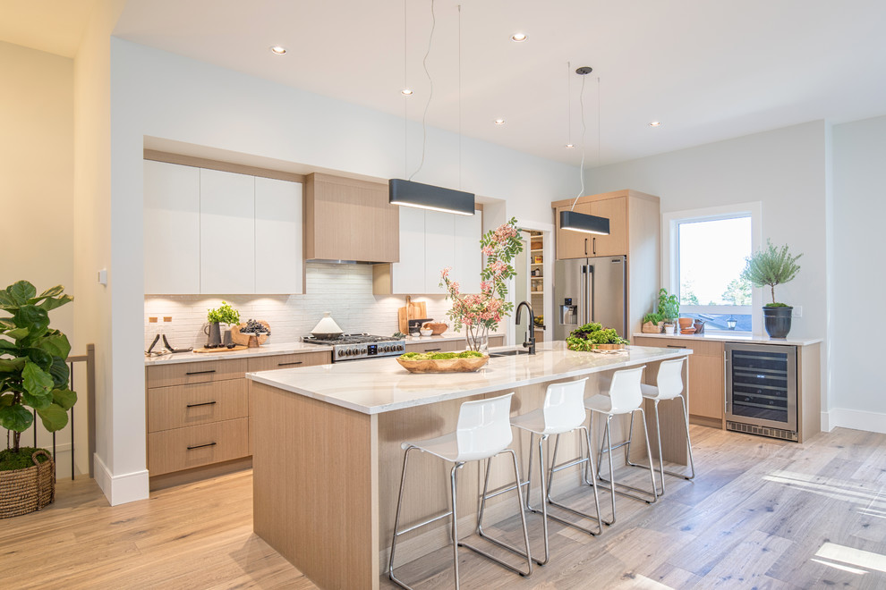 Large trendy l-shaped light wood floor and beige floor kitchen photo in Vancouver with an undermount sink, flat-panel cabinets, light wood cabinets, white backsplash, stainless steel appliances, an island and white countertops