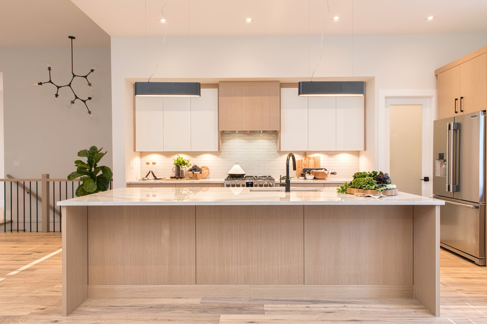 Large contemporary kitchen in Vancouver with a submerged sink, flat-panel cabinets, light wood cabinets, engineered stone countertops, beige splashback, ceramic splashback, stainless steel appliances, light hardwood flooring, an island, beige floors and white worktops.