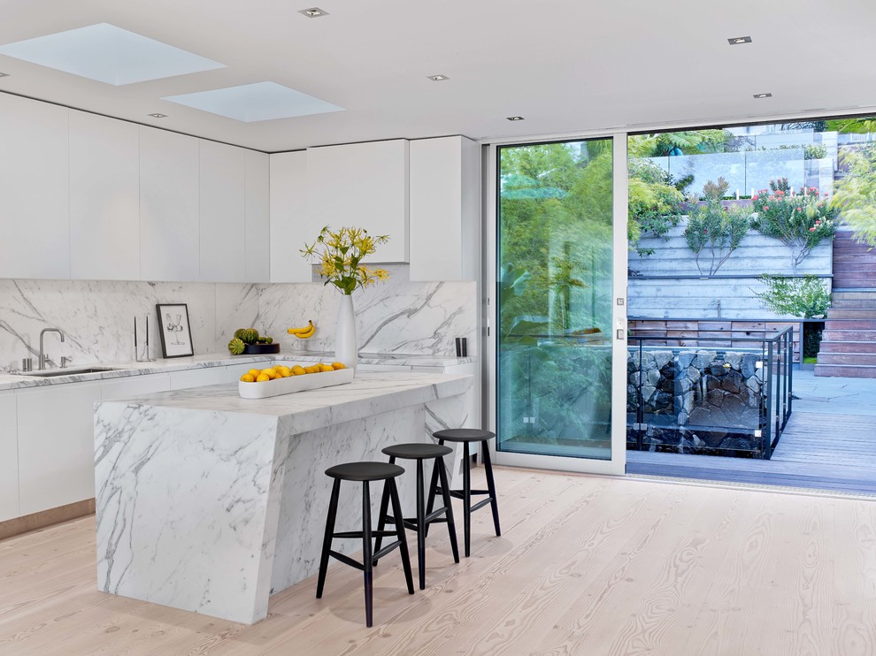 Photo of a contemporary l-shaped kitchen in San Francisco with flat-panel cabinets, white cabinets, white splashback, light hardwood flooring and an island.