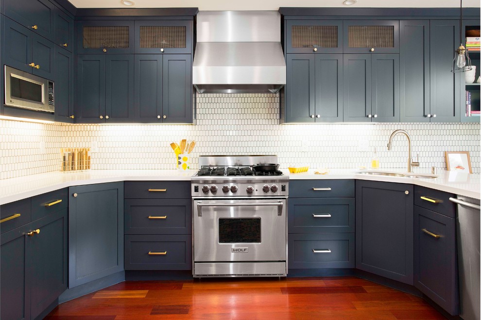 Inredning av ett modernt stort kök, med en dubbel diskho, skåp i shakerstil, blå skåp, bänkskiva i kvarts, vitt stänkskydd, stänkskydd i keramik, rostfria vitvaror, mellanmörkt trägolv och en halv köksö