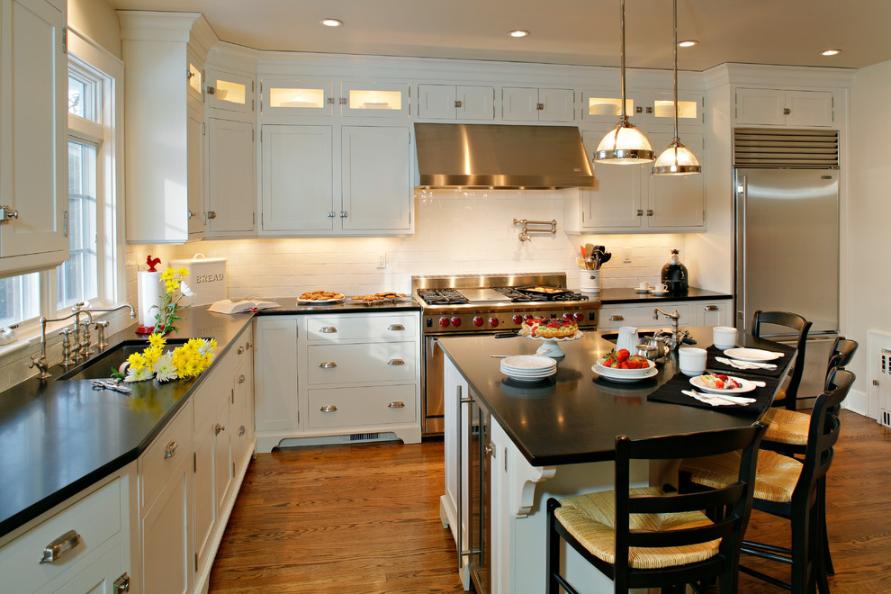 Klassisk inredning av ett mellanstort kök, med en undermonterad diskho, skåp i shakerstil, vita skåp, granitbänkskiva, vitt stänkskydd, stänkskydd i tunnelbanekakel, rostfria vitvaror, mellanmörkt trägolv, en köksö och brunt golv