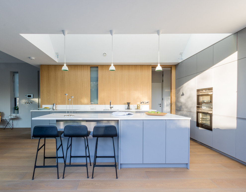 На фото: кухня среднего размера в современном стиле с плоскими фасадами, серыми фасадами, черной техникой, светлым паркетным полом, островом и врезной мойкой