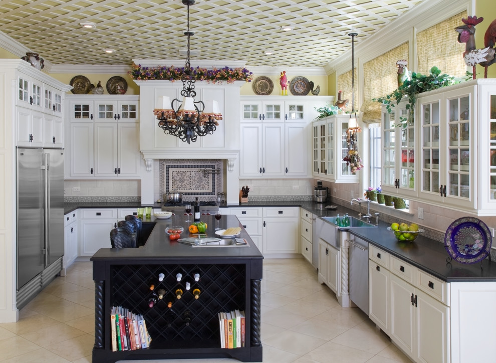 Klassisk inredning av ett stort kök, med en rustik diskho, luckor med profilerade fronter, vita skåp, granitbänkskiva, beige stänkskydd, stänkskydd i mosaik, rostfria vitvaror, kalkstensgolv och en köksö