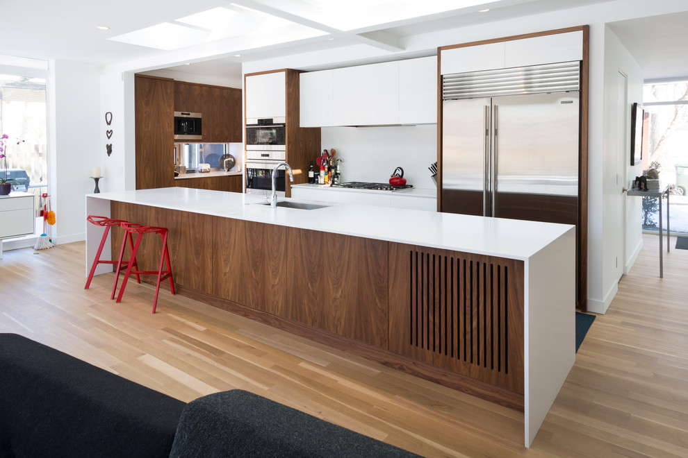 Contemporary kitchen in Chicago with a submerged sink, flat-panel cabinets, medium wood cabinets, composite countertops, stainless steel appliances and an island.