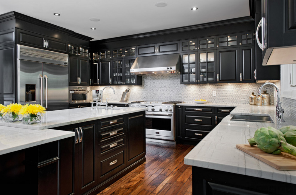 Inspiration for a large farmhouse l-shaped kitchen/diner in Orange County with a belfast sink, raised-panel cabinets, black cabinets, engineered stone countertops, grey splashback, ceramic splashback, stainless steel appliances, dark hardwood flooring and an island.
