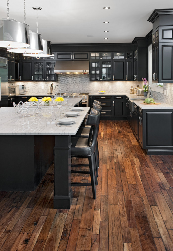 This is an example of a large rural l-shaped kitchen/diner in Orange County with a belfast sink, raised-panel cabinets, black cabinets, engineered stone countertops, grey splashback, ceramic splashback, stainless steel appliances, dark hardwood flooring and an island.
