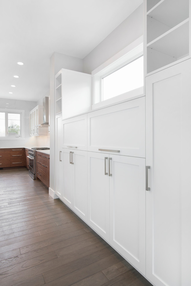 Photo of a large contemporary single-wall kitchen pantry in Calgary with a submerged sink, shaker cabinets, stainless steel cabinets, engineered stone countertops, white splashback, ceramic splashback, stainless steel appliances, dark hardwood flooring and an island.