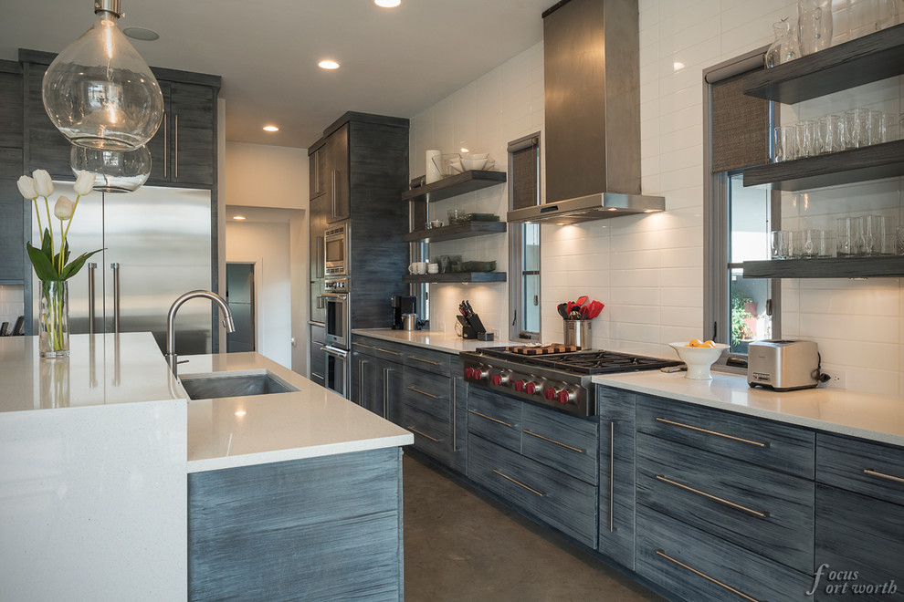 Inspiration for a mid-sized modern galley concrete floor open concept kitchen remodel in Dallas with an undermount sink, flat-panel cabinets, gray cabinets, white backsplash, subway tile backsplash, stainless steel appliances and an island