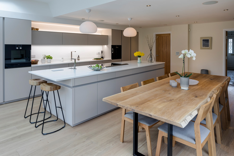 Inspiration for a medium sized contemporary single-wall kitchen in West Midlands with flat-panel cabinets, white cabinets, white splashback, integrated appliances, an island, beige floors and white worktops.