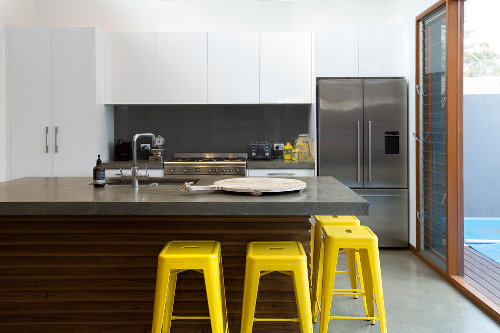 Idéer för ett mellanstort modernt kök, med en undermonterad diskho, släta luckor, vita skåp, bänkskiva i betong, grått stänkskydd, glaspanel som stänkskydd, rostfria vitvaror, betonggolv och en köksö