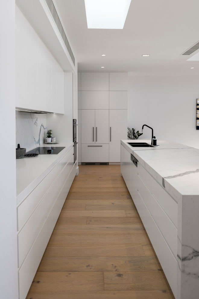 Inspiration for a mid-sized scandinavian single-wall medium tone wood floor and brown floor open concept kitchen remodel in Adelaide with a double-bowl sink, white cabinets, marble countertops, white backsplash, marble backsplash, black appliances, an island and white countertops